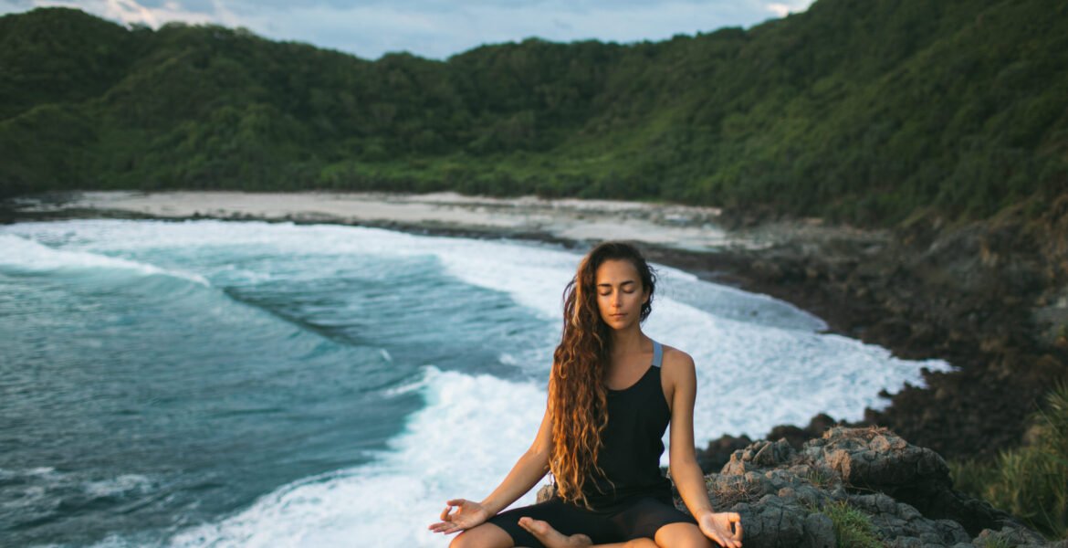 Young woman practicing yoga in lotus pose at sunset with beautif