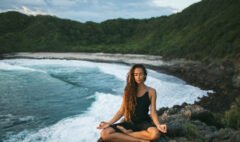 Young woman practicing yoga in lotus pose at sunset with beautif