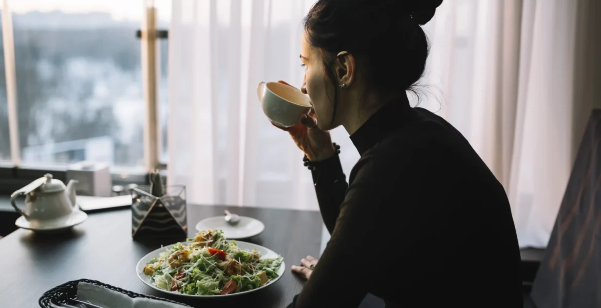 young-woman-drinking-from-cup-table-with-salad-near-window_11zon