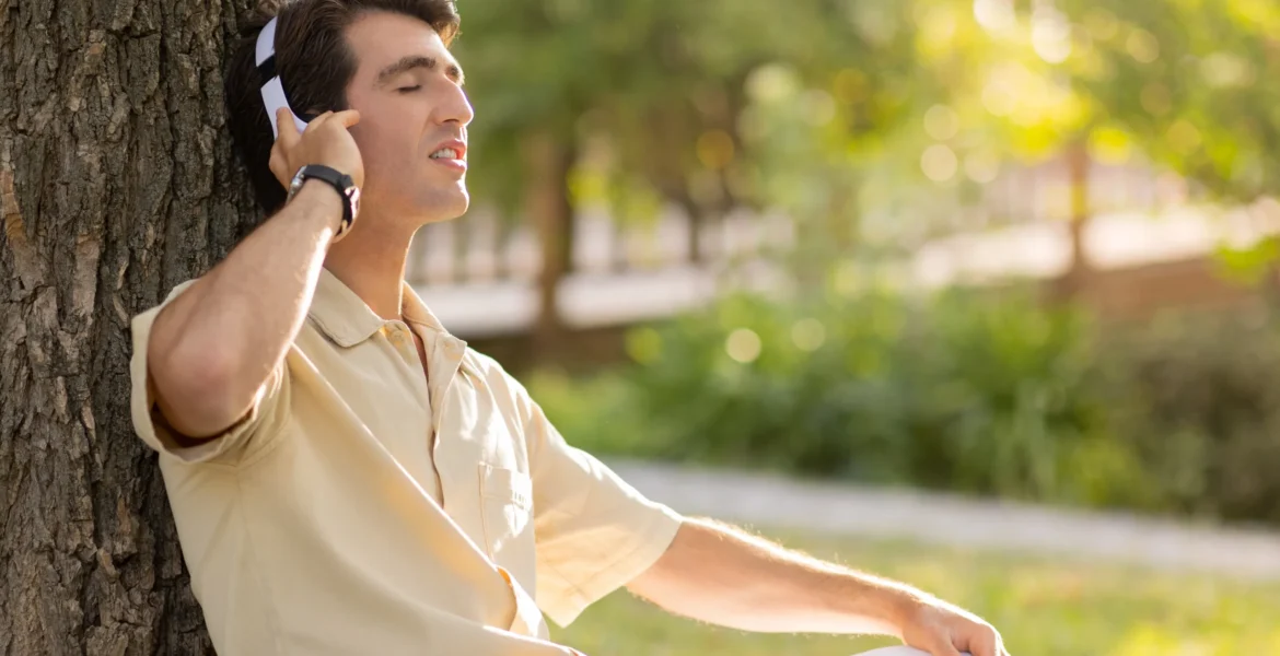 joyful-young-caucasian-man-listening-music-park