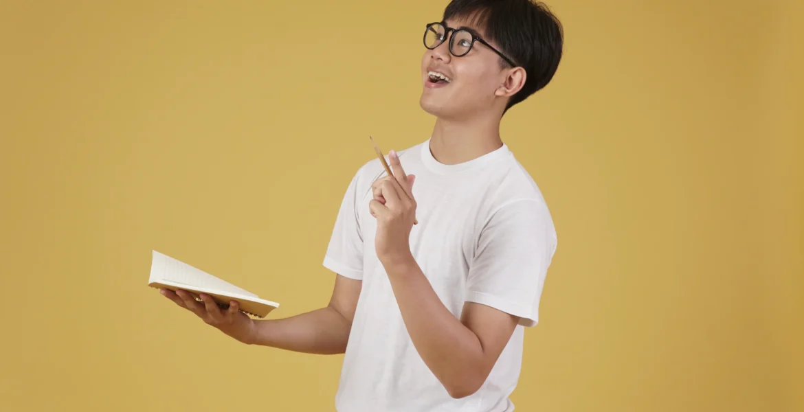 happy-cheerful-young-asian-man-student-dressed-casually-wearing-eyeglasses-pointing-finger-up-having-idea-isolated